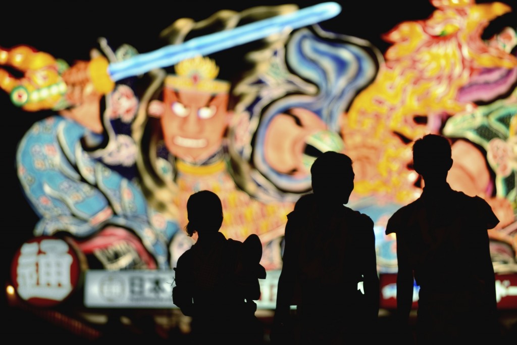 The summer Nebuta festival in Aomori city features giant floats parading through the street at nighttime.