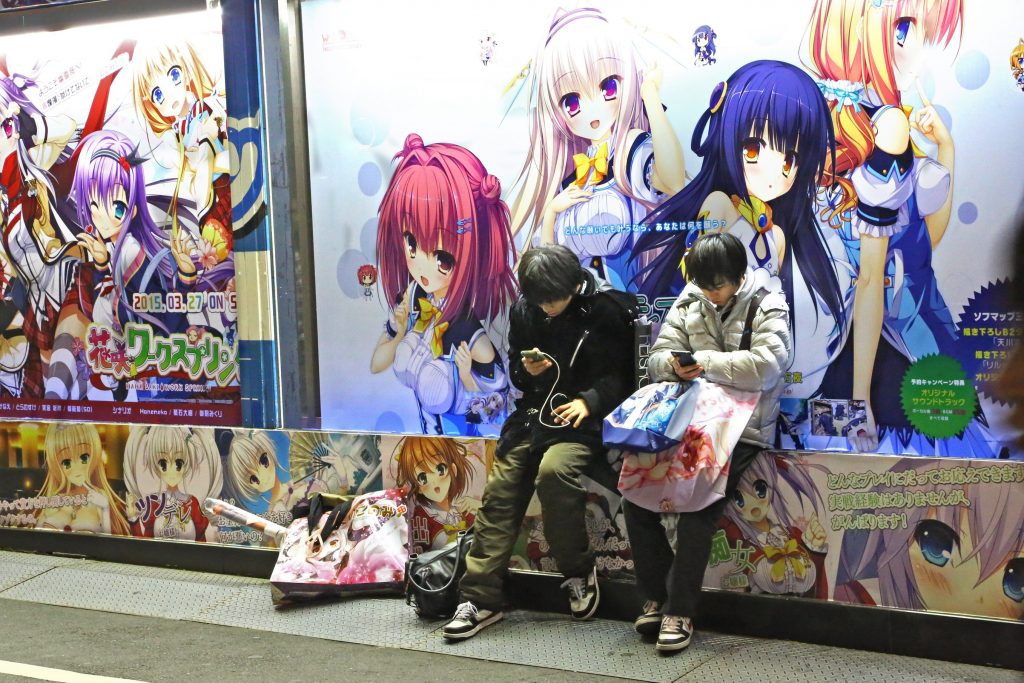 Tokyo, Japan - December 30, 2014: two teenagers use their portables in Akihabara district. On the wall behind them drawings of Manga.