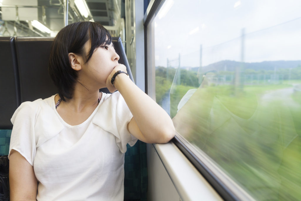 A young Japanese woman is traveling in a train and looking at the rural scene outside of the window.